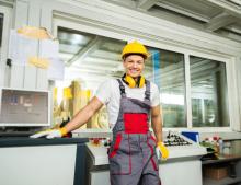 A white construction person stands smiling, seeming ready and enthusiastic to work on their next project.